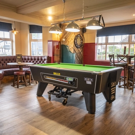 An image of the interior restaurant seating and games area with tables, chairs, cushioned corner seating, pool table, dartboard and wooden flooring at The Sportsman.