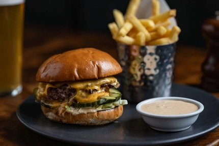 An advertising image showing a burger and fries dish sat on a wooden table.