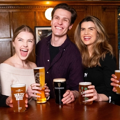 An image of a group of friends stood at an interior table enjoying drinks while watching a football match shown on TV within an Urban Social venue.
