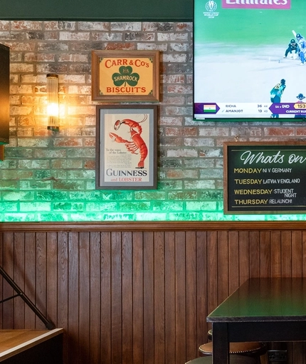 The interior seating area at Molly Malones, with wooden furniture, a TV on the wall, and a small stage area in the corner.