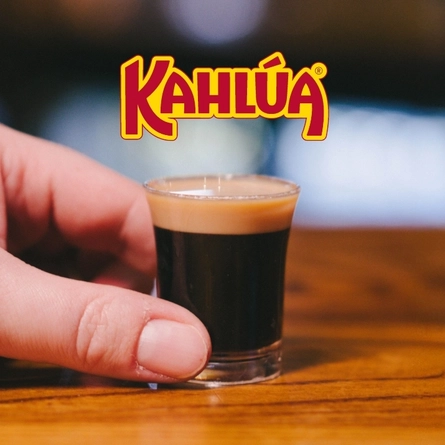 A banner showing the Kahlua logo next to a hand holding a shot glass containing a Baby Guinness.