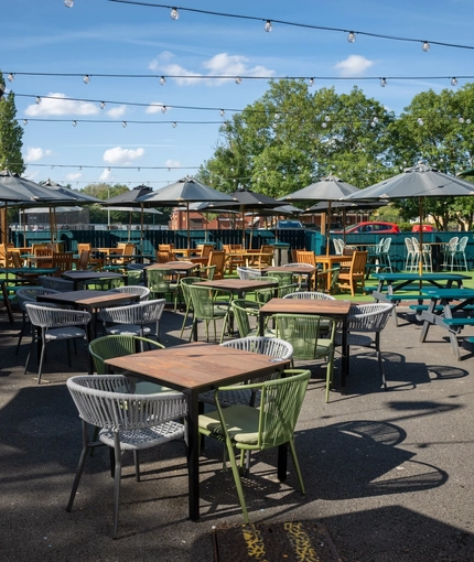 The exterior beer garden seating area at the Rudds Arms in Marton-In-Cleveland; with shade umbrellas on some of the tables, and string lights overhead.