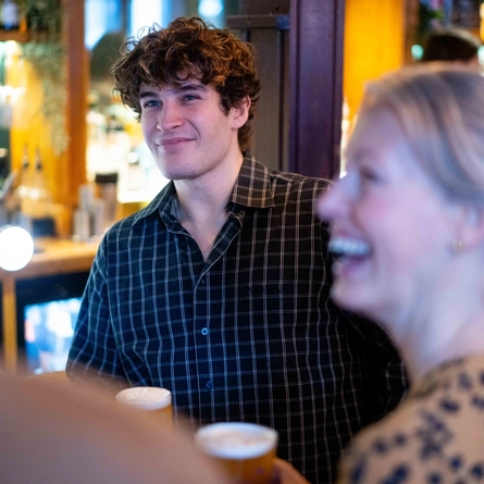 An image focusing on a person within a group stood at the interior bar with drinks at an Urban Social venue.
