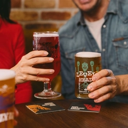 People at a pub table holding drinks, including a pint of Level Head beer and a glass of red Old Mout cider, with other drinks in the foreground.
