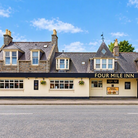 The exterior facade of the venue with venue signage, advertising signage and hanging baskets at The Four Mile Inn.