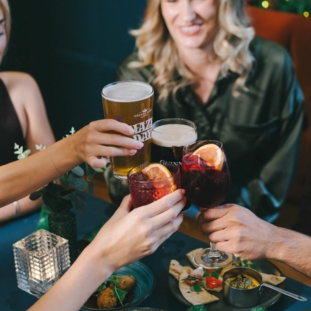 An image of 4 friends celebrating a cheers with a selection of drinks while enjoying various sides sat within the interior restaurant seating area.
