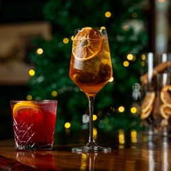 Two cocktail type drinks on a bar.  One in a low ball tumbler and the other is in a stemmed glass.