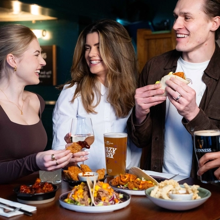 An image of a group of friends stood at a table within the restaurant area with a small plates dishes and drinks available at Urban Social venues.