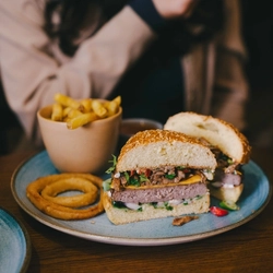 A product image showing a plated burger dish and a cocktail style drink sat on a table within the interior restaurant seating area at an Urban Core venue.