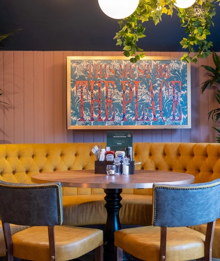 An interior restaurant seating area at the Tredegar Arms, with an upholstered semi-circular booth seat, potted plants behind the seat, and framed artwork on the wall.