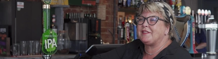 A person resting on a bar while speaking to someone.