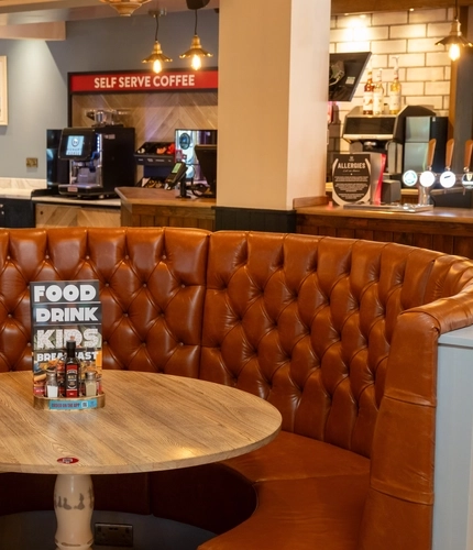 A circular restaurant booth seat surrounding a small wooden table, in the bar area of The Weathervane.