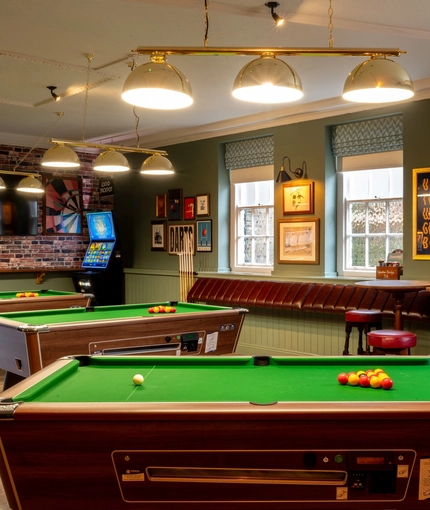 The interior gaming area at the Wooden Bridge in Guildford, with pool tables, TVs on the walls, a gaming machine, and seating areas.