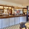 A close up view of the bar inside The Flying Horse in Heald Green. Behind the bar are bottles of wine and spirits on wooden shelves, as well as a slushie machine.