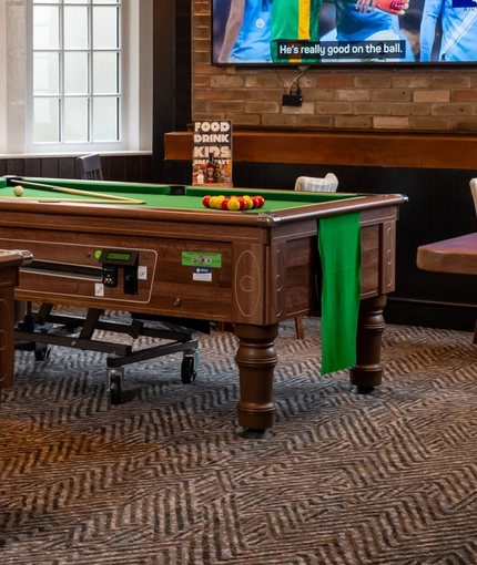 The interior pub gaming area of The Railway, with two pool tables, a TV on the wall, and restaurant tables.