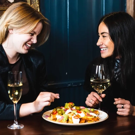 Two people share a plate of nachos and white wine in the pub