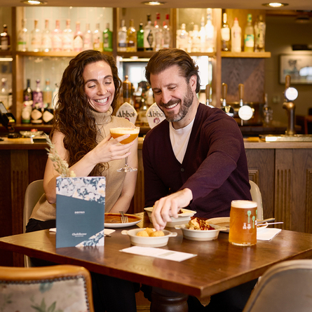An image of 2 friends sat at a table within the interior restaurant seating area enjoying drinks and a selection of picky bits at a Chef & Brewer venue.