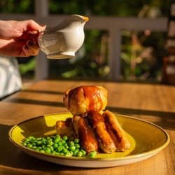 A served main of sausage and mash with a customer pouring gravy available at Hungry Horse venues.