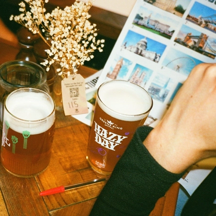 A image focusing on papers from a quiz night event set up at the seating area in a Greene King London venue with a pint of Level Head and Hazy Day served on the table.