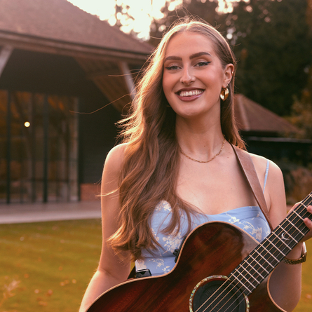 An image of Ellen Blane holding a guitar to advertise a live music What's On event at The Cart & Horses.