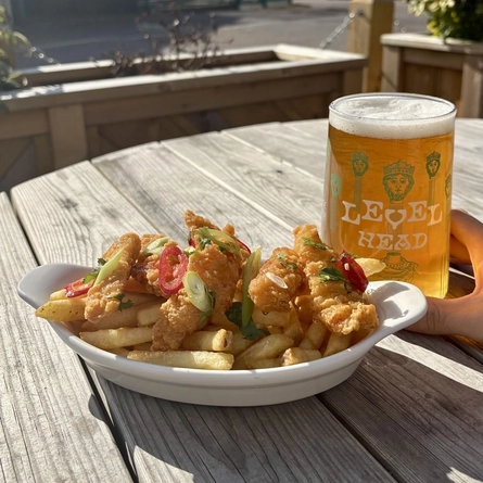 A roasting dish with fries next to a pint of Level Head on a table outside.
