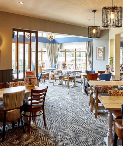 The interior restaurant seating area of The Flying Horse in Heald Green, featuring wooden tables, upholstered chairs and artwork on the walls.