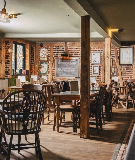 The interior restaurant seating area at Ye Olde Swan in Thames Ditton, with exposed brick walls, wooden beams, and framed artwork on the walls.