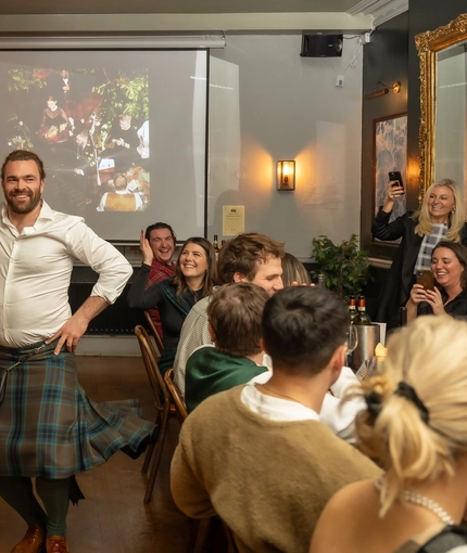 An image of people sat at tables clapping as a person in a traditional Scottish outfit dances within the interior function room during a Burns Night Event at The Crabtree.