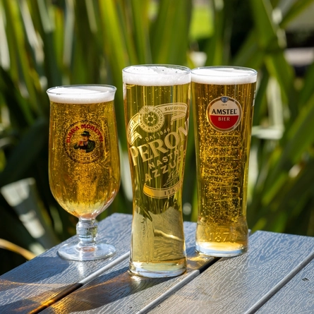 An advertising image showing a pint of Amstel, a pint of Peroni and a pint of Birra Moretti sat on an exterior wooden table.