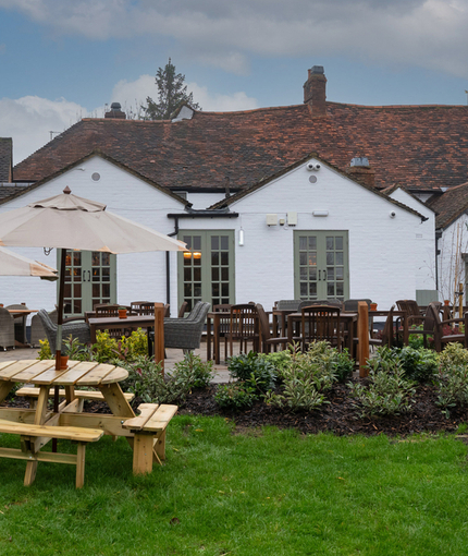 The exterior facade, signage, and beer garden seating area of Ye Olde Swan, with picnic tables and shade umbrellas.