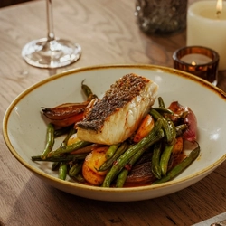An advertising image of a Roasted Coley dish and a glass of white wine within the interior restaurant seating area at The Foundry Bell.