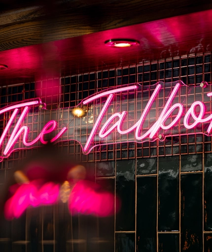 A close up view of a neon pink sign spelling "The Talbot" in cursive lettering; on a wall inside The Talbot.