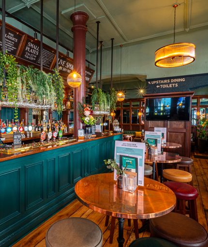 The bar and interior restaurant seating area at The Fountains Abbey, with a TV on the wall and plants hanging above the bar.