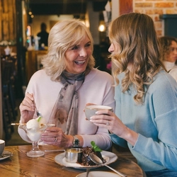 A lifestyle image of 2 ladies enjoying Mothers Day dessert dishes and hot drinks within the interior restaurant seating area at a Pub & Grill venue.