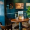 The interior restaurant seating area of the Cock & Pye, with wooden furniture, a large potted plant, and framed artwork on the wall.