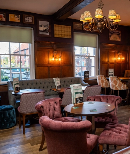 The interior restaurant seating area at The Fox in Bury St Edmunds, with wood panelled walls, upholstered chairs, and framed artwork on the walls.