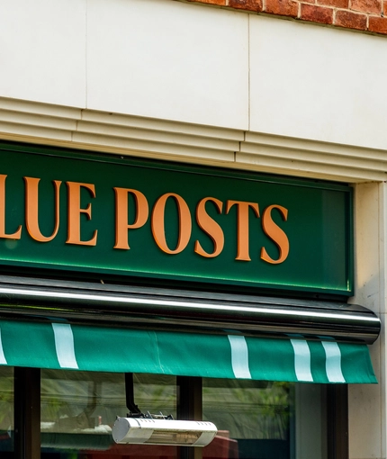 A close up view of the exterior signage of the Blue Posts in St James's, with the words "Blue Posts" in golden yellow capital letters on a dark green panel above the window.