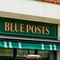 A close up view of the exterior signage of the Blue Posts in St James's, with the words "Blue Posts" in golden yellow capital letters on a dark green panel above the window.