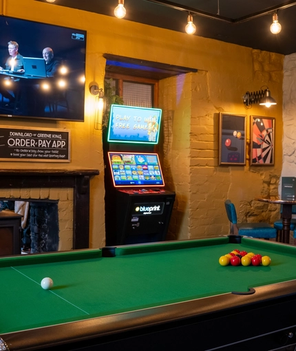 The interior gaming area at the Tredegar Arms in Bassaleg, with a pool table, a fireplace, a TV on the wall, a gaming machine, and a small restaurant table.