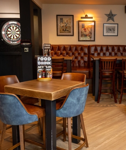 An interior restaurant seating area at The Wall's End in Wallsend, with upholstered booth seating, an illuminated dartboard, and framed artwork and football shirts on the walls.