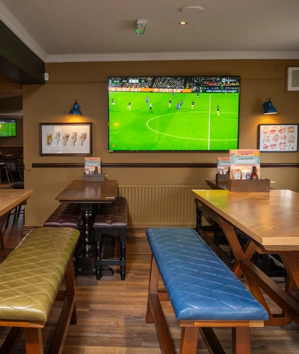 An interior restaurant seating area at The Longship, with upholstered bench seats, and a TV on the wall.
