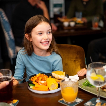An image of a family enjoying various dishes and drinks within the interior restaurant seating area at a Community Pubs With Food venue.