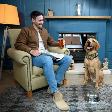 A man drinking a pint in the pub with his dog sat next to him