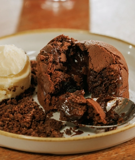A lifestyle image of a plated Chocolate Fondant dessert dish from the Valentines Day menu sat on a table within the interior restaurant seating area at The Crown.