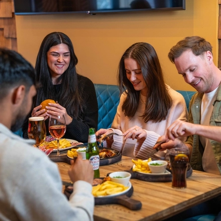 An image showing a group of people sat around a table enjoying mains dishes and drinks at a Flaming Grill venue.