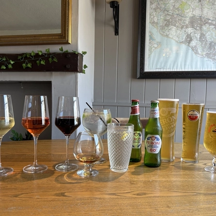 An image showing a selection of drinks including zero alcohol drinks, lagers, wines, spirits and cocktails served in glasses and bottles sat on a wooden table to advertise Happy Hour at Venture HOtels.