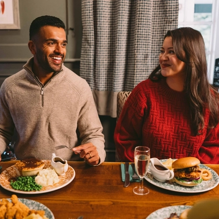 A group of people seated at a festive decorated table near a Christmas three. There are plates of food and drinks in front of them.