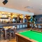 Interior dining area of a pub with a bar, a TV, a fireplace, a pool table and a few dartboards.