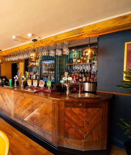 The wood panelled bar and interior restaurant seating area at The Windmill Inn in York, with wine glasses hanging in racks above the counter, and a TV on the wall.
