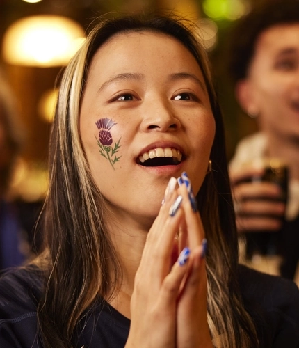 An image of a woman wearing a sport team shirt, watching a sporting event.